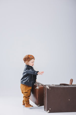 A happy boy in a helmet and a pilot's jacket carries a brown suitcase. Portrait of a child pilot, a child in a leather jacket. Little traveler with a suitcaseの写真素材