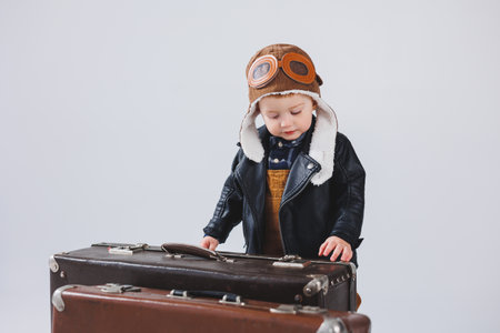 Happy little boy with a brown suitcase. Portrait of a child tourist, a child in overalls. Little traveler with a suitcaseの写真素材