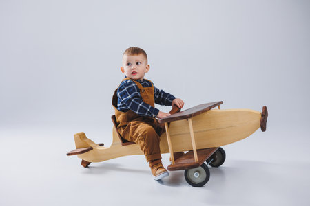 A 3-year-old boy in a checkered shirt sits on a large wooden plane. Children's environmentally friendly toys from woodの写真素材