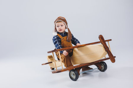 Little boy 3 years old plays with a wooden plane on a white background. In overalls and a pilot's hat. Children's eco toys made of natural wood. wooden planeの写真素材