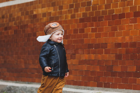 Stylish boy 3 years old in a leather jacket and brown trousers walks on the street. Modern child. Children's fashion. Happy childの写真素材