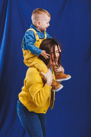 A young mother plays with her child on a blue background. Family relationship with the child. Raising a child, playing with a childの写真素材