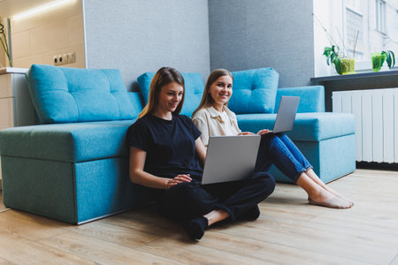 Two cute women working using laptop in living room on sofa. Friends, friendship, time together....