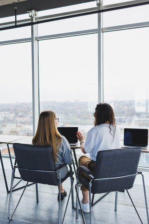 Beautiful two young confident business women sitting in an office room working on a laptop computer. The work of colleagues in a modern office.の写真素材