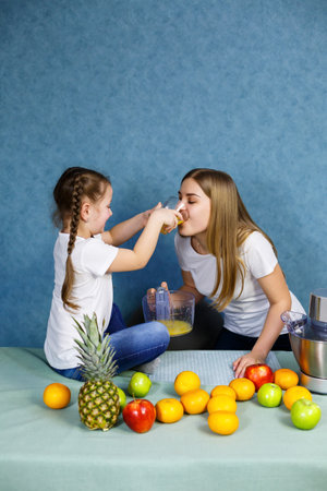 Little girl and mom squeeze fresh juice from fruits and drink it.の写真素材