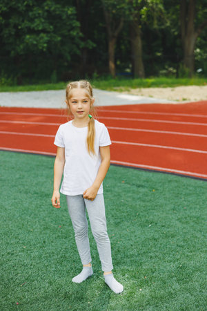 A little girl goes in for sports on the grass, the child does a warm-up before training at the stadium. Children's sports and healthy lifestyle.の写真素材