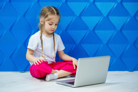 7 years old girl in a white T-shirt sits on the floor with a laptop and presses the keysの写真素材