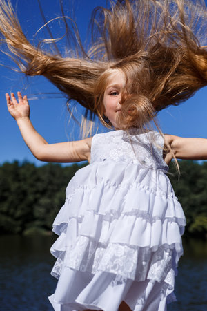 A six year old girl is wearing a white dress. Beautiful long hair. Walk near the river on the background of the forestの写真素材