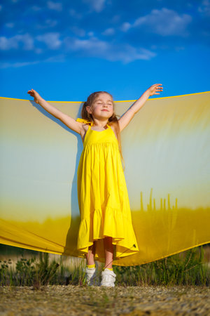 Ukrainian girl 7 years old, she is a patriot of Ukraine, dressed in a yellow dress against a blue sky. Blue sky. Sunny day. Free Ukrainian child. Child symbol of Ukraineの写真素材