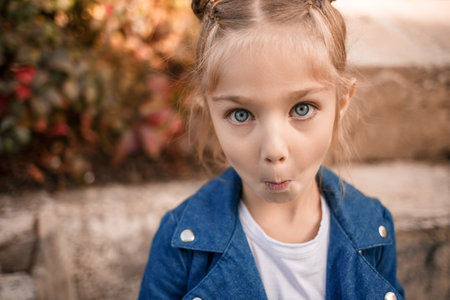 A beautiful girl of about seven in a denim jacket looks at the camera and makes facesの写真素材