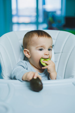 Little adorable baby eating avocado. Vitamin and healthy food for small children. Portrait of beautiful child of 8 monthsの写真素材