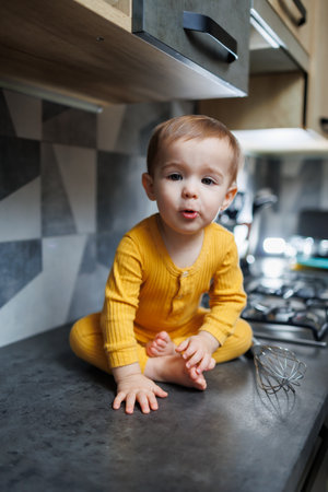 A little boy 1 year old in yellow clothes is sitting in the kitchen on the table. Portrait of a cute one-year-old boy.の写真素材