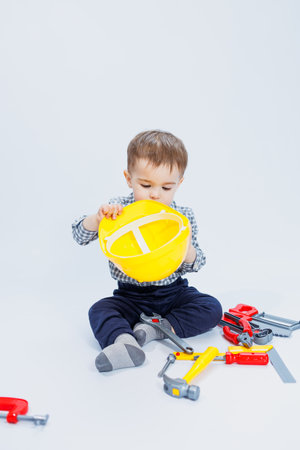 A little boy in a checkered shirt in the image of a builder. A boy in a construction helmet and plastic toolsの写真素材
