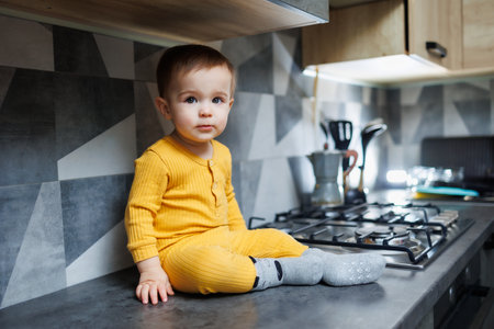 A little boy 1 year old in yellow clothes is sitting in the kitchen on the table. Portrait of a cute one-year-old boy.の写真素材