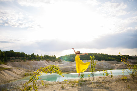 Young woman in a yellow dress near the lake with azure water and green trees.の写真素材