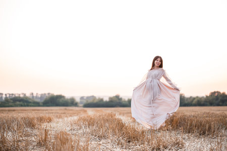 A pregnant woman on the background of a field at sunset, a woman with long hair and a belly spread her arms to the sides and enjoys the freedom of the wind.の写真素材