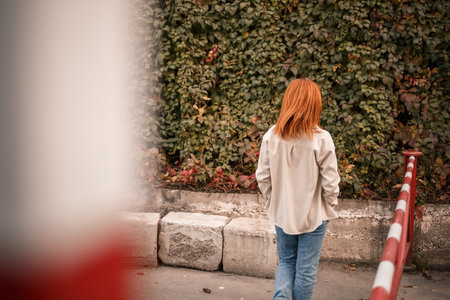 A pretty redhead young woman is walking down the street, she is dressed in jeans and a beige shirt. Beautiful girl dressed in casual style with a smile on her faceの写真素材