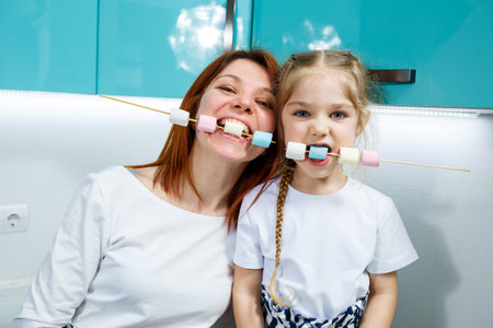 Mom with daughter in the turquoise kitchen eat marshmallows. Lovely family relationships. Happy family concept, happy parents and childrenの写真素材