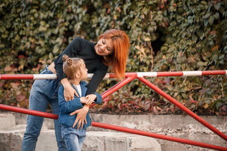 Stylish red-haired mother and her daughter are talking warmly. Happy child and her mom on the street. Successful single mother with her daughter for a walk. Warm family relationshipの写真素材