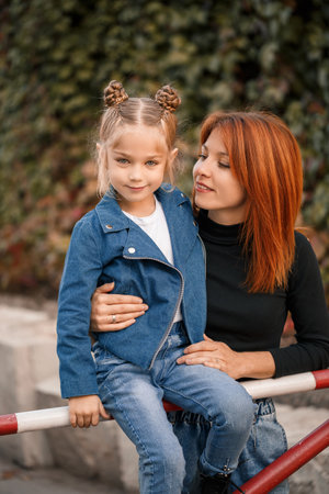 Stylish red-haired mother and her daughter are talking warmly. Happy child and her mom on the street. Successful single mother with her daughter for a walk. Warm family relationshipの写真素材