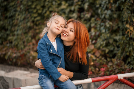 Stylish red-haired mother and her daughter are talking warmly. Happy child and her mom on the street. Successful single mother with her daughter for a walk. Warm family relationshipの写真素材
