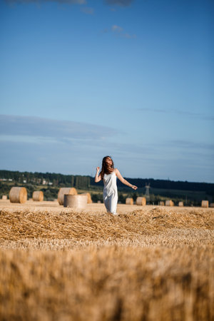 Young curly-haired woman in a wheat field, where there is a huge sheaf of hay, enjoying nature. People and travel. Nature. sun rays Agricultureの写真素材