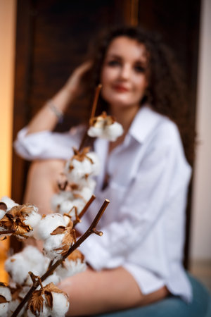 Close-up portrait of her, she is beautiful, attractive, lovely, cheerful, with wavy hair, girl having fun, smiling, on a light, pastel background, white flowers, white shirtの写真素材