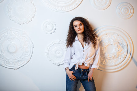 Beautiful young girl model with curls posing. She is wearing a white shirt and jeans.の写真素材