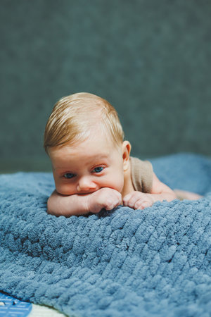 A small newborn boy lies on a gray knitted blanket. Portrait of a one-month-old baby