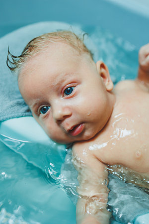 Bathing a two-month-old baby in a bathtub, the child lies on a plastic stand. Baby care.