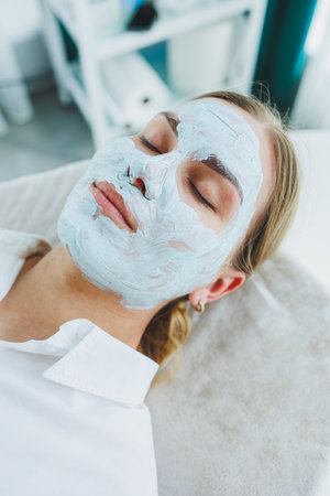 Young beautiful woman smiling with cream on her face. Care mask for facial skinの写真素材