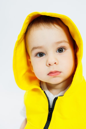 Little cheerful boy 1 year old in a yellow vest on a white background. Children's bright clothes. Portrait of a cheerful child in a hoodの写真素材