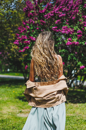 A beautiful curly woman in a summer dress runs and rejoices, she is wearing sunglasses. Against the background of a purple lilac bushの写真素材