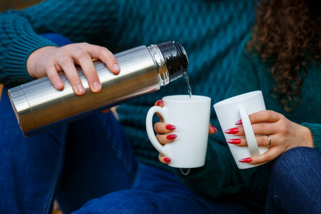 Couple in sweaters drinks tea in the autumn forestの写真素材