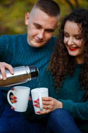 Couple in sweaters drinks tea in the autumn forest
