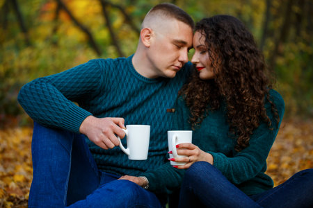 Couple in sweaters drinks tea in the autumn forest