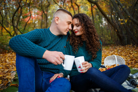 Couple in sweaters drinks tea in the autumn forestの写真素材