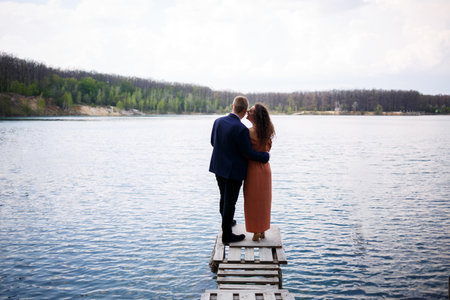 A young couple holding hands on a wooden bridge in the middle of a blue lake. Masonry on the island on a background of trees. Nature, landscape. Romance and love, happy coupleの写真素材