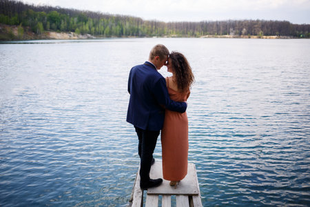 A young couple holding hands on a wooden bridge in the middle of a blue lake. Masonry on the island on a background of trees. Nature, landscape. Romance and love, happy coupleの写真素材