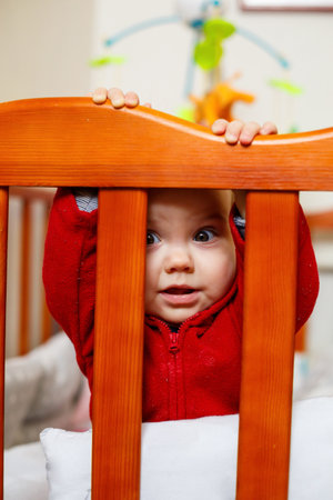 little child girl in a red sweater, smiles beautifully, in a crib, plays and has fun, emotional photoの写真素材