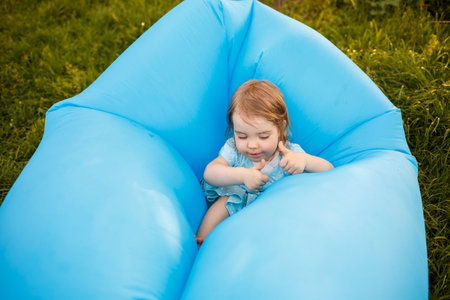 A beautiful little girl is resting and playing in the fresh air. Fooling around on a blue inflatable...