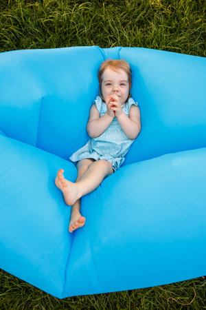 A beautiful little girl is resting and playing in the fresh air. Fooling around on a blue inflatable...
