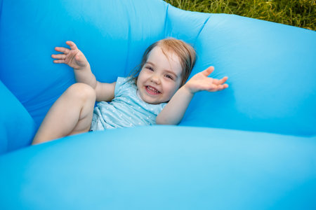 A beautiful little girl is resting and playing in the fresh air. Fooling around on a blue inflatable mattress. Smiles and rejoicesの写真素材