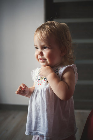 A little girl of 1.5 years is standing and smiling. The child dances and walks. Cheerful girl in the...
