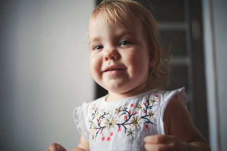 A little girl of 1.5 years is standing and smiling. The child dances and walks. Cheerful girl in the apartmentの写真素材