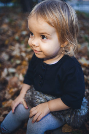 A little girl of 1.5 years is standing and smiling. The child throws leaves. Cheerful girl in the autumn forestの写真素材