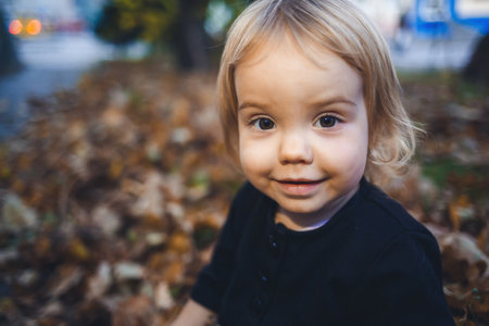 A little girl of 1.5 years is standing and smiling. The child throws leaves. Cheerful girl in the autumn forestの写真素材