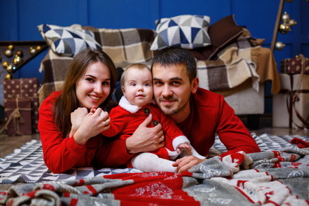 A happy family in red sweaters is sitting together on the floor. Christmas holiday atmosphere. A...