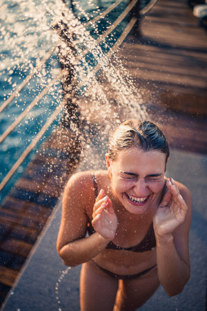Beautiful young woman takes a relaxing shower in a swimsuit on a sunny day outdoors by the sea. The girl on vacation is resting. Selective focusの写真素材