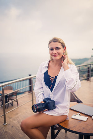Beautiful woman photographer blogger on vacation, working with laptop by the pool. Freelance remote...